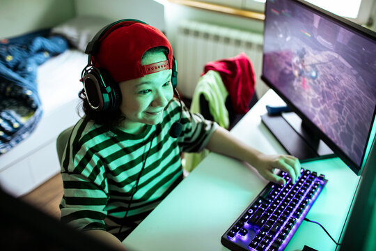 Smiling young gamer with headset playing pc game at home