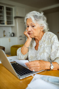 Senior woman reviewing bills on laptop at home