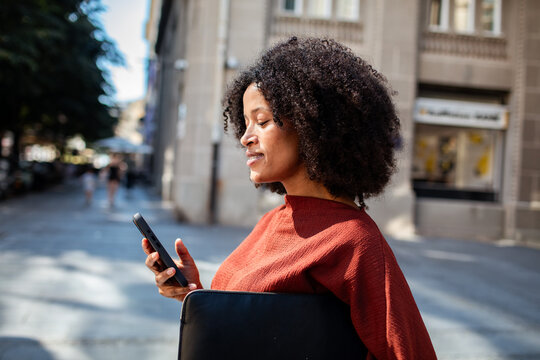 Confident young woman using smartphone on city street