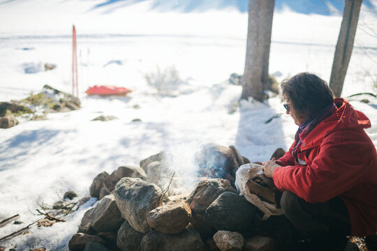 Mature woman sitting beside stone fire pit in snowy landscape