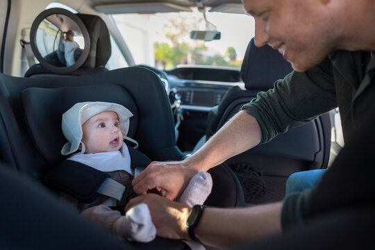 Father strapping his baby safely into black car seat