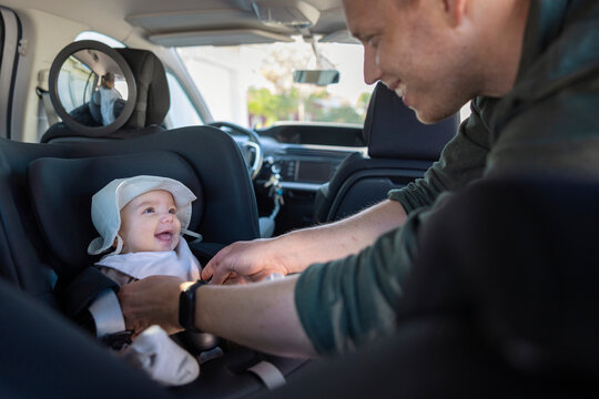 Father playing with his cute toddler son sitting in car seat during family trip