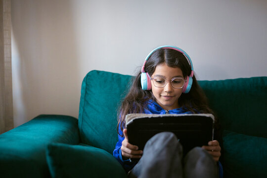 Girl sitting on sofa using digital tablet for online learning at home