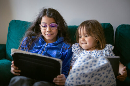 Happy siblings sharing digital tablet while relaxing on sofa at home