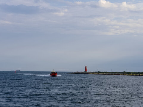 Boats travel on water near a red lighthouse during late afternoon hours