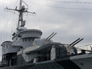 Historic naval ship docked in a port on a cloudy day with visible turrets and equipment © Piotr