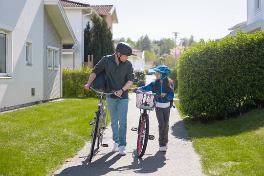 Father and daughter talking with each other while while wheeling their bicycles on path