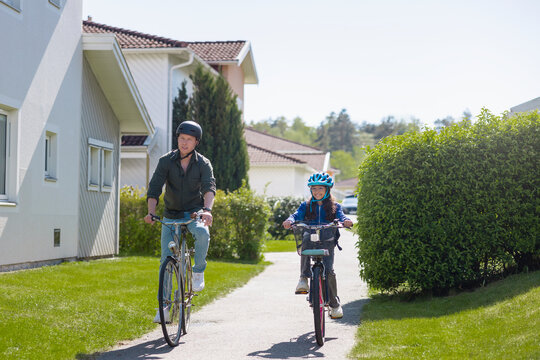 Father and daughter cycling on sunny path in neighborhood