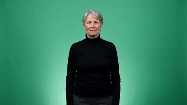 Mature woman in black turtleneck standing calmly against a solid green backdrop with soft lighting