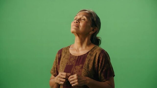 Middle-aged woman with closed eyes and serene expression, standing against a green background