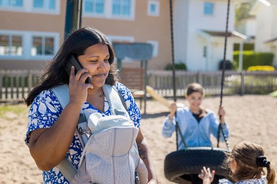 Mother talking on smart phone while carrying her baby at playground