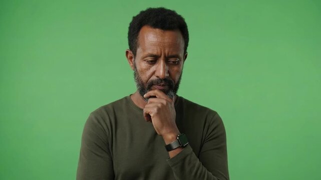 Thoughtful middle-aged man with beard pondering solutions against a solid green background