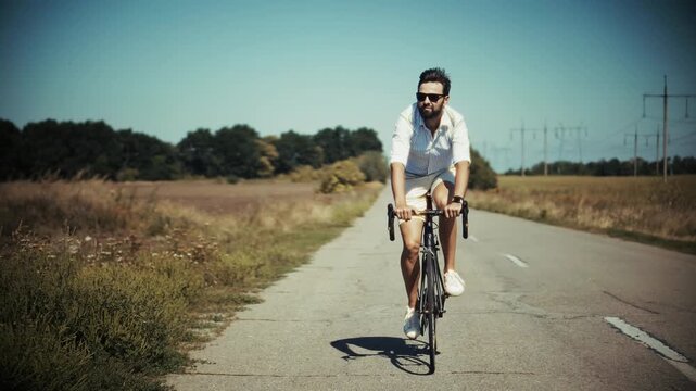 Cyclist Riding Bicycle Along Countryside Road On Sunny Day