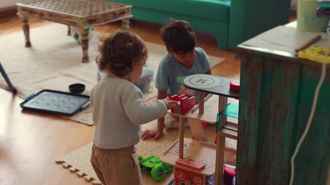 Toddler standing near older brother while interacting with toy garage playset capturing sibling connection, shared play and authentic indoor childhood activity at home