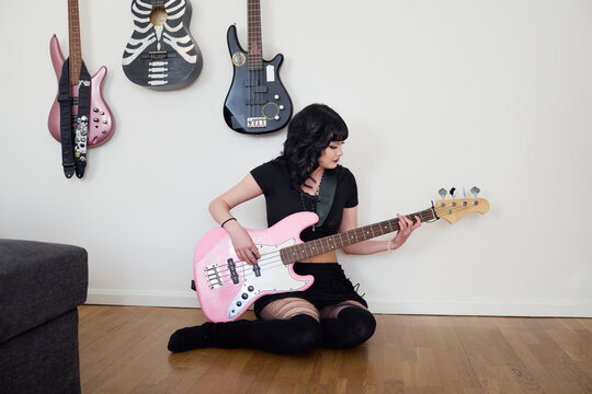 Full length of punk woman playing guitar while sitting on floor against wall