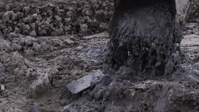 Raw industrial energy and relentless earth-moving force dominate the scene; dark, clumped soil and rugged machinery convey heavy labor and extraction
