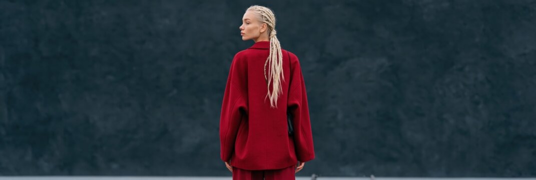 Wide panorama rear view of woman with long braided hair in oversized red coat for fashion banner and minimalist background