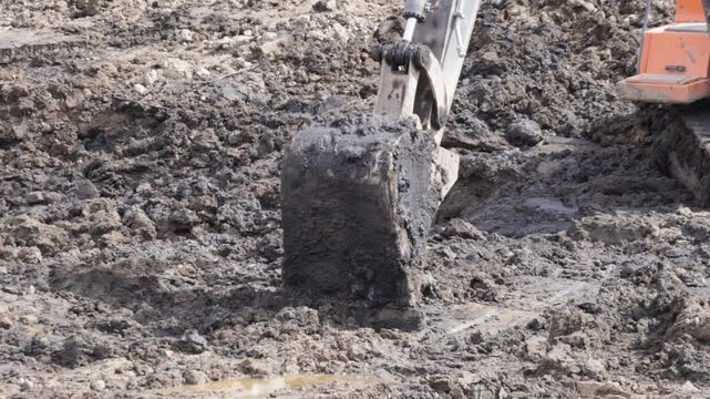 Raw industrial energy and relentless earth-moving force dominate the scene; dark, clumped soil and rugged machinery convey heavy labor and extraction