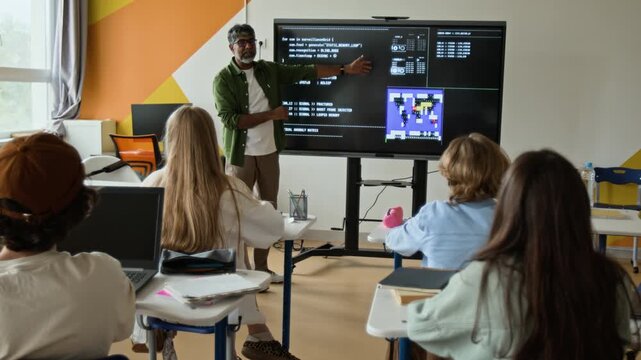 Indian middle aged teacher explaining programming code on interactive screen to teenagers in classroom, zooming out. Footage is suitable for STEM education and school promo videos