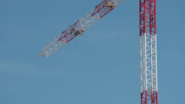 Tower crane operating with its long jib moving against a clear blue sky background