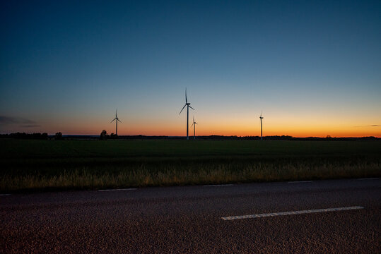 Distant in silhouette view of wind turbines on meadow against moody sky