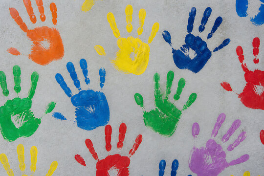 Colorful handprints are scattered across a light-colored, textured surface.