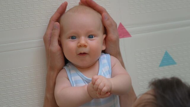 Father gently stroking baby son's head on soft mat. Close-up. Slow motion.