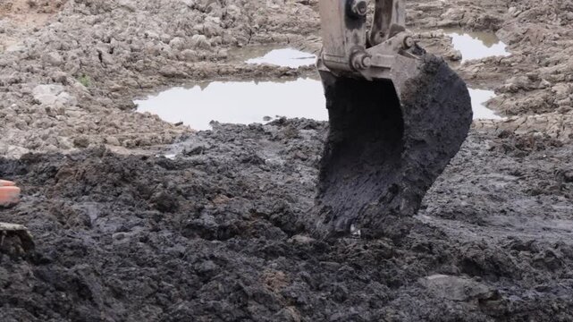 Raw industrial power meets stubborn, saturated soil; thick mud clings to the bucket as the machine wrestles the unyielding terrain