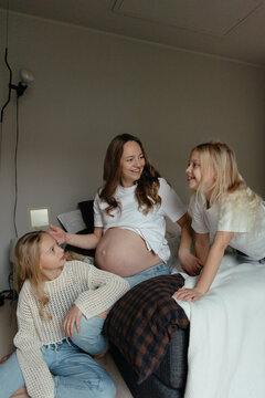 Smiling pregnant mother spending leisure time with daughters in bedroom at home