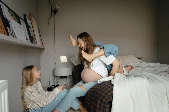 Happy pregnant woman enjoying leisure time playing with daughters in bedroom at home