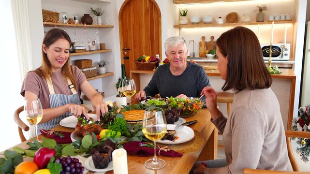 A family Christmas and Thanksgiving party: parents and daughter have dinner together at the dining table, eating roast chicken, pie, and drinking wine and cheers. 