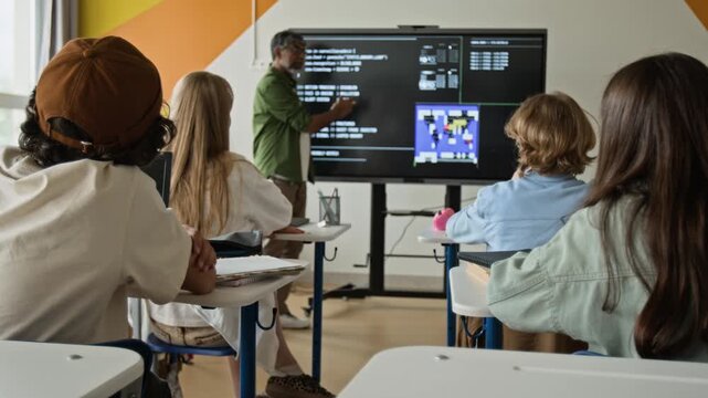 Rear view of multiethnic teenagers sitting at desks, raising hands during coding lesson with multiethnic teacher. Ideal for promoting STEM education and modern learning programs