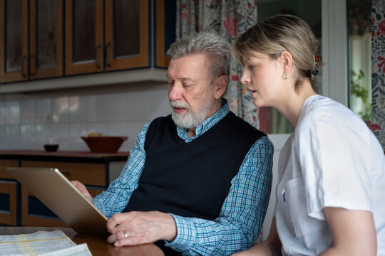 Female nursing assistant helping senior man in reading news on tablet PC at home