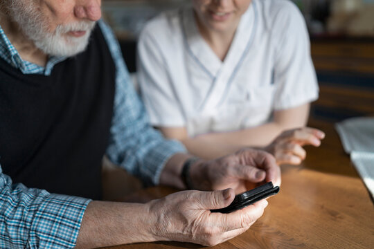 Senior man using smart phone while sitting with female nursing assistant at table in home