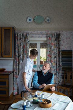 Senior man asking help of female nurse while using tablet PC during breakfast at home