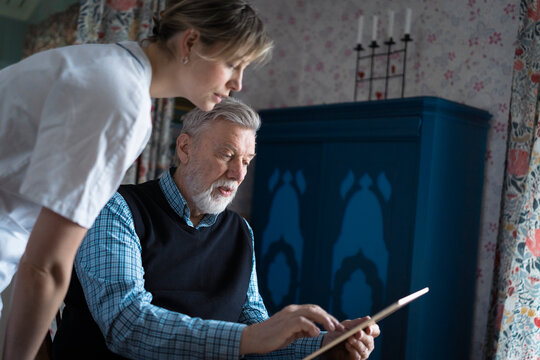 Senior man getting assistance of female nurse in using tablet PC at home
