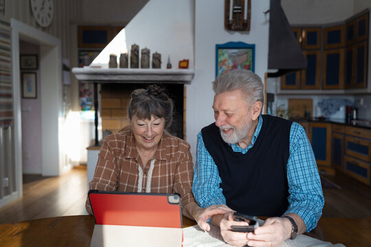 Couple spending leisure time solving crossword puzzle together on digital tablet while sitting at table in home