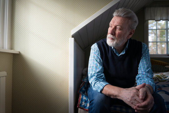 Contemplative senior man looking away while sitting on bed in home