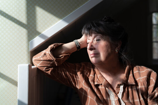 Sad mature woman leaning on bed while sitting lonely in bedroom at home