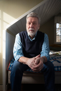 Portrait of elderly man sitting on bed in bedroom at home