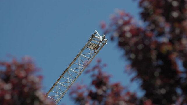 Construction crane jib arm slowly swaying against a clear blue sky, seen through red autumn leaves