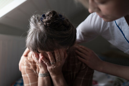 Female healthcare worker consoling mature woman crying in bedroom at home