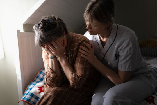 Female nursing assistant consoling mature woman crying in bedroom at home