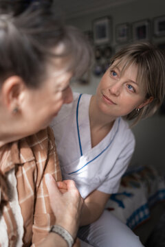 Female medical expert consoling sad woman while sitting in bedroom during house call