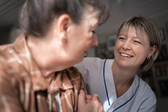 Smiling female medical expert cheering sad woman during house call