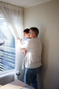 Father carrying son while looking out through window at home