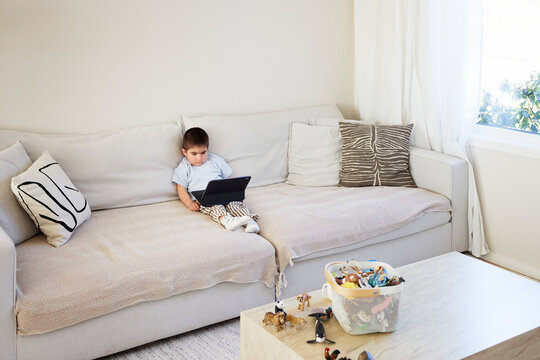 Boy sitting with laptop on sofa in living room at home