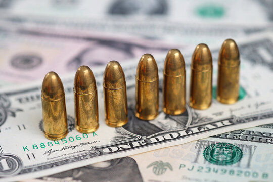 Row of ammunition cartridges standing on US dollar banknotes. Concept of financial crime, armed conflict, illegal money, organized crime, violence, security threats and weapon financing.