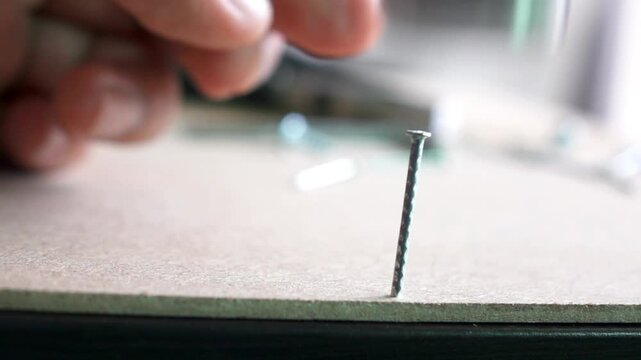 Hammering nail close up hand using hammer to stuck nail into wood surface in carpentry workshop in 4K Ultra HD footage.
