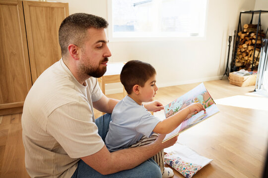 Father reading picture book for son while sitting in living room floor at home